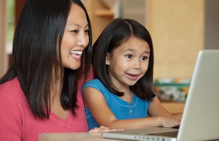 Mom with young daughter smiling looking at laptop