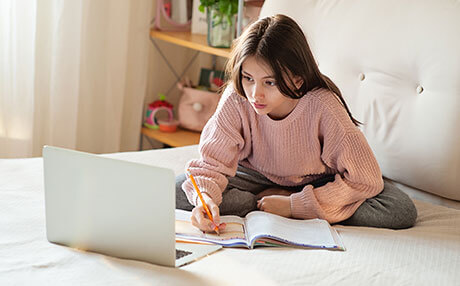 Young girl writing on a notebook and looking at laptop at home