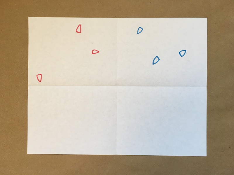 A paper folded horizontally and vertically, with red ships drawn in the upper left and blue ships drawn on the upper right